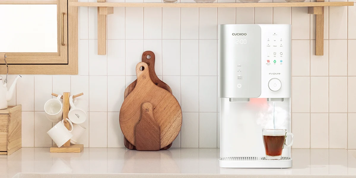 Cuckoo Inspire water purifier dispensing hot water into a glass mug on a kitchen counter. (cp-sn102hw)