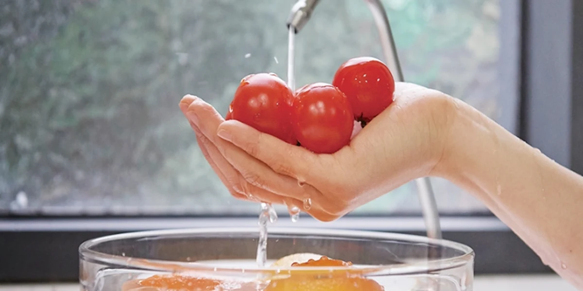 Washing cherry tomatoes in a hand under a stream of purified water above a glass bowl. (cp-sn102hw)