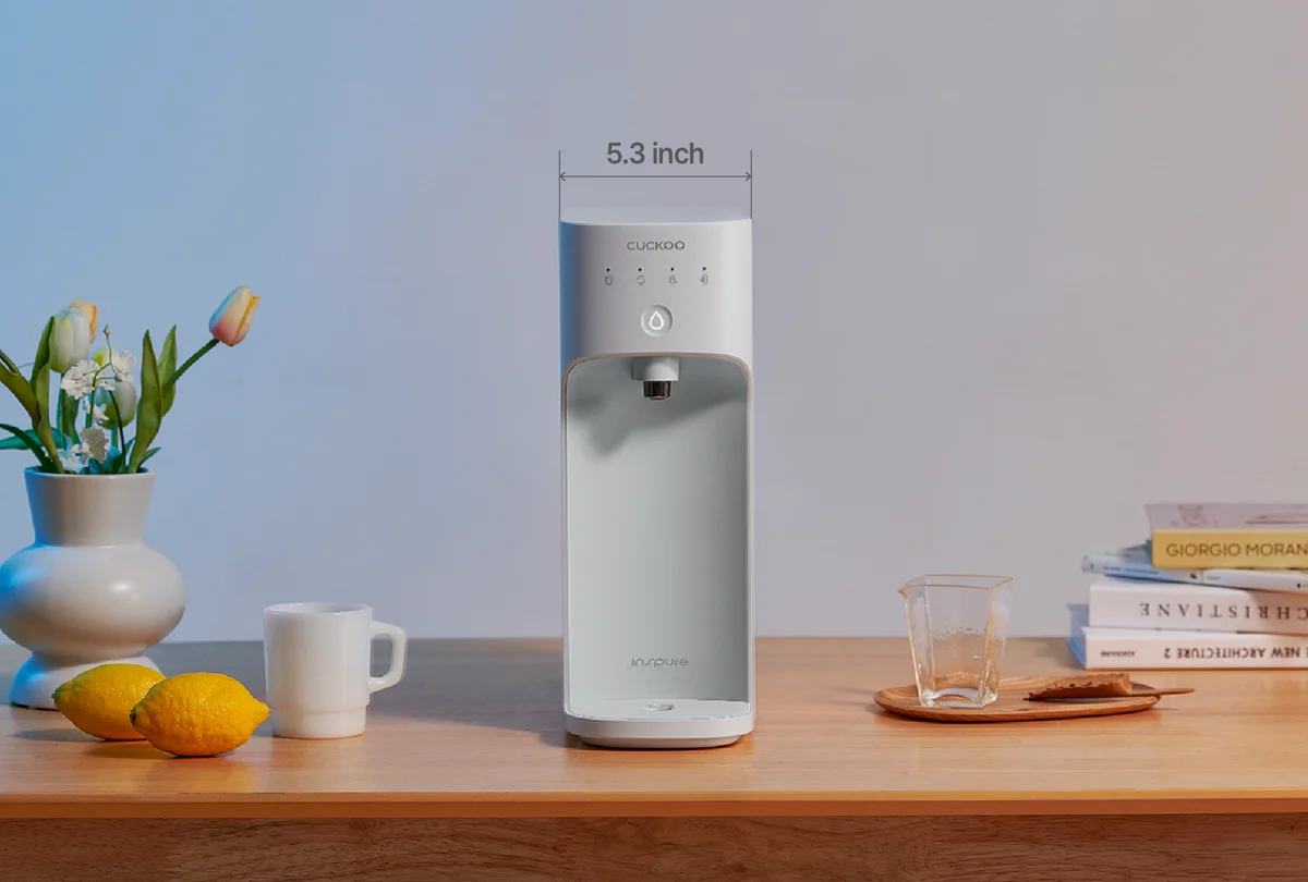 CUCKOO INPURE water purifier on a kitchen table, front view showing 5.3-inch width with lemons, mugs, and books. (CP-AKN011)