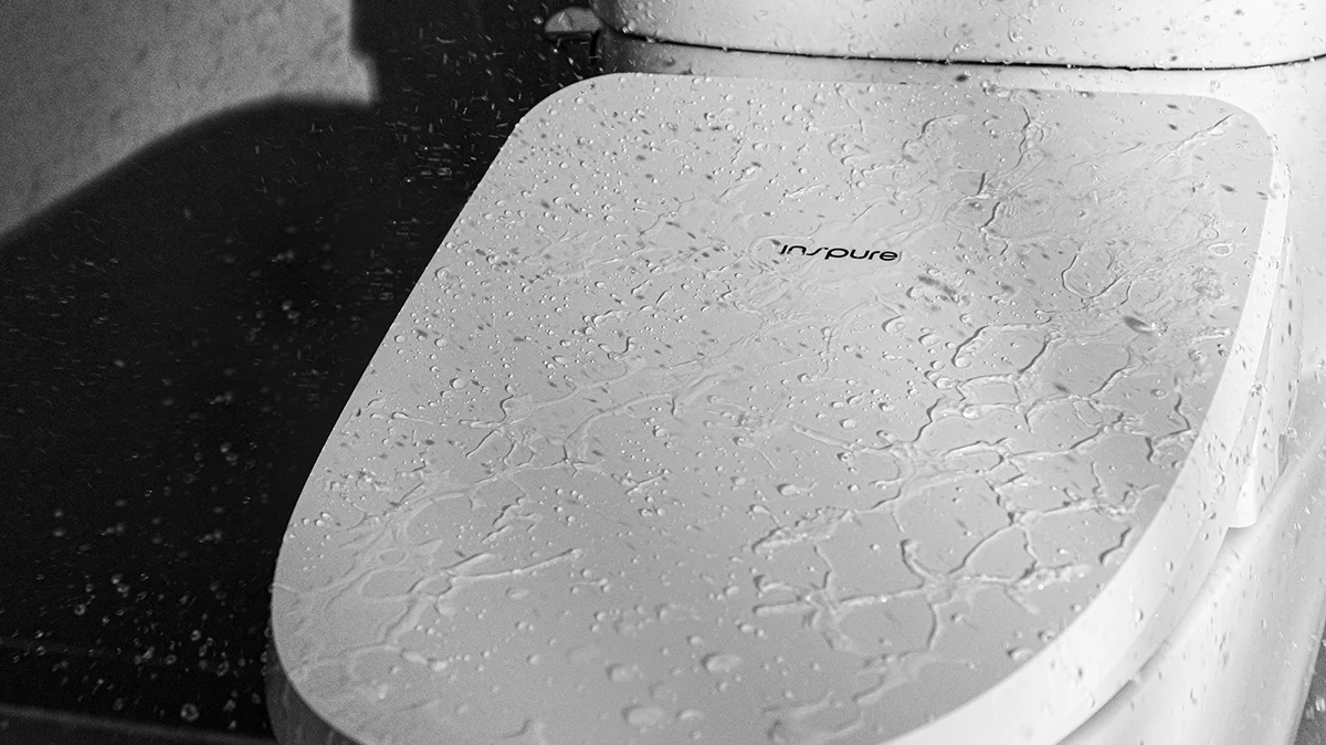 Inspure bidet seat lid covered in water droplets, demonstrating its water-resistant surface during cleaning. (CBT-I1030RW)